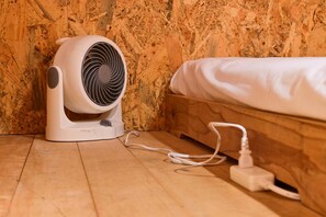 Een witte, draagbare verwarming met snoer aangesloten op een stopcontact, op een houten vloer, naast een bed met een witte matras.
