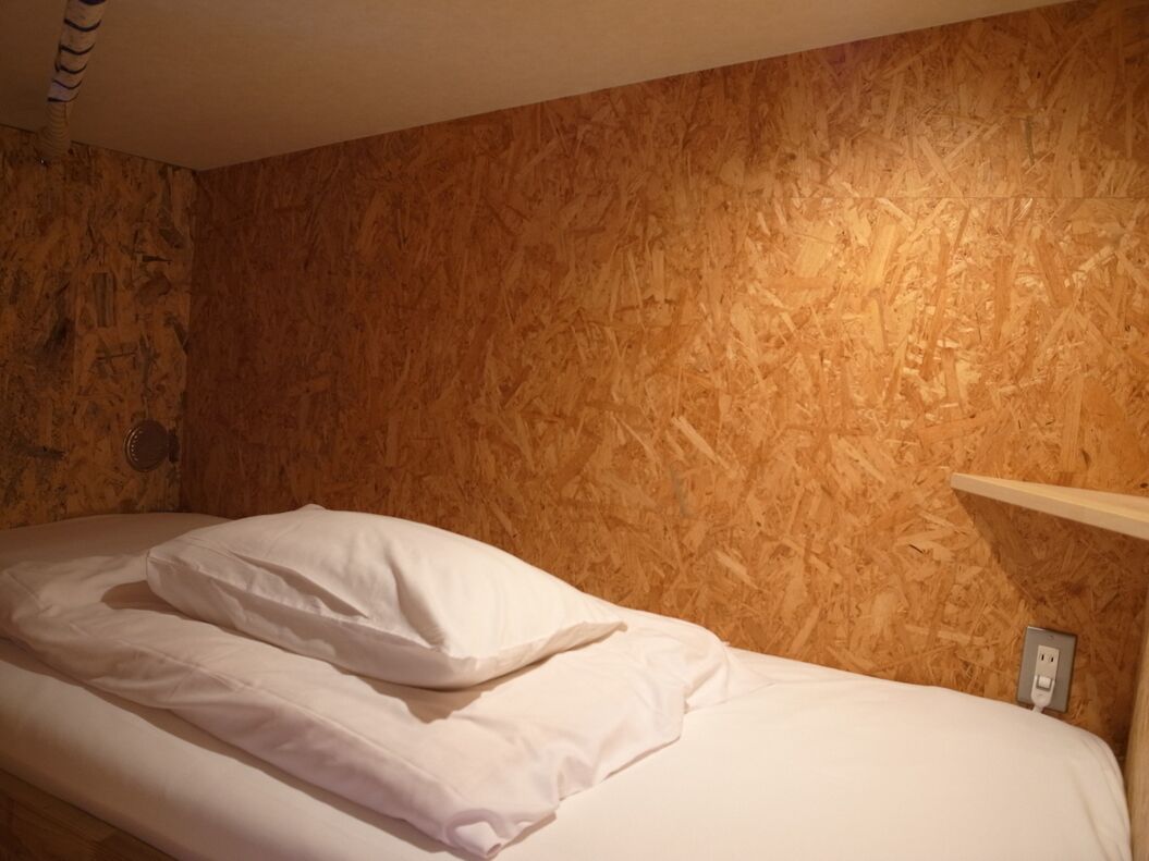 Un lit simple avec une literie blanche, dans une pièce dont les murs sont recouverts de panneaux de bois.