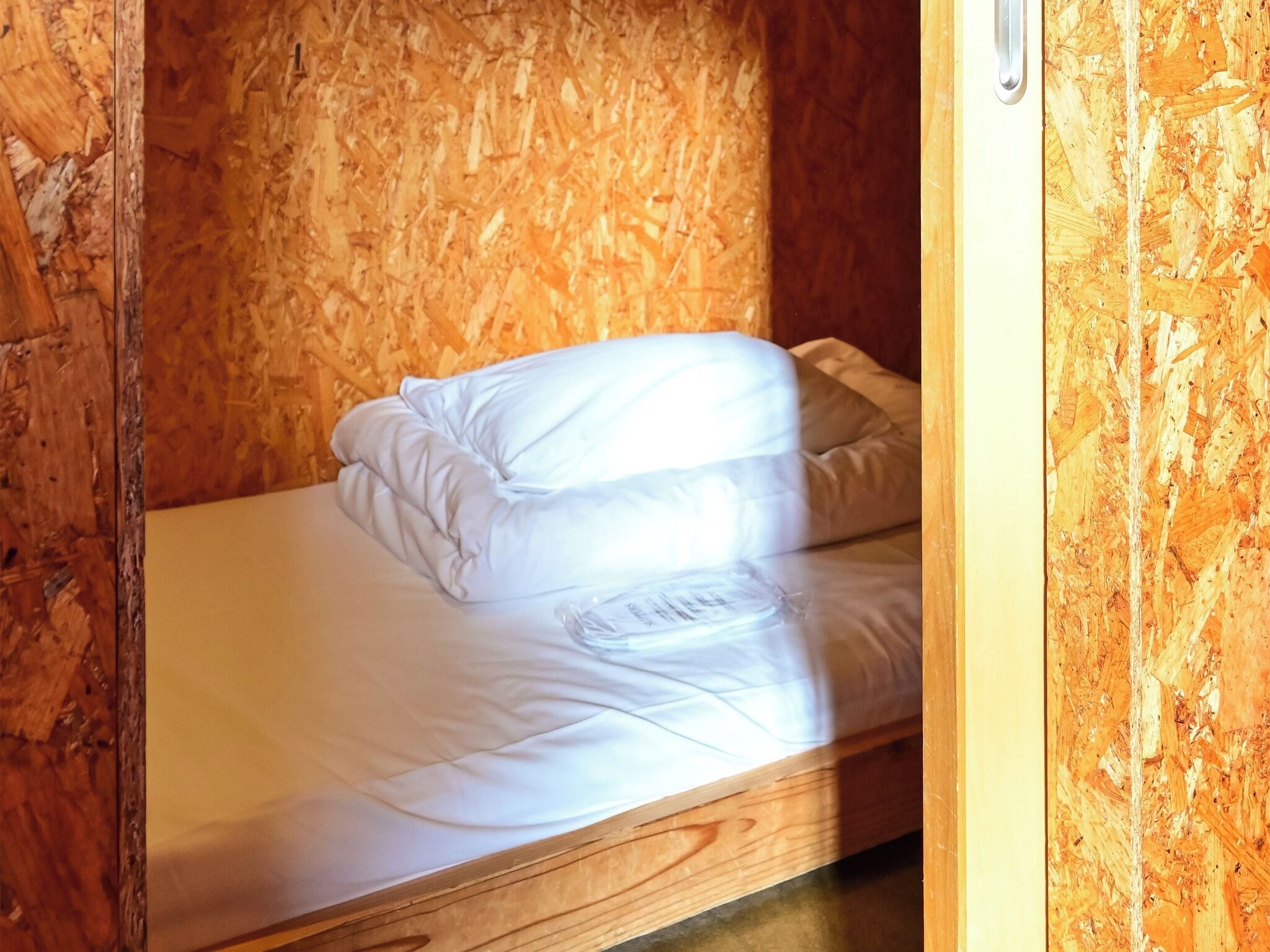 Ein Einzelbett mit weißer Bettwäsche in einem Zimmer mit Holzwänden und Holzboden.