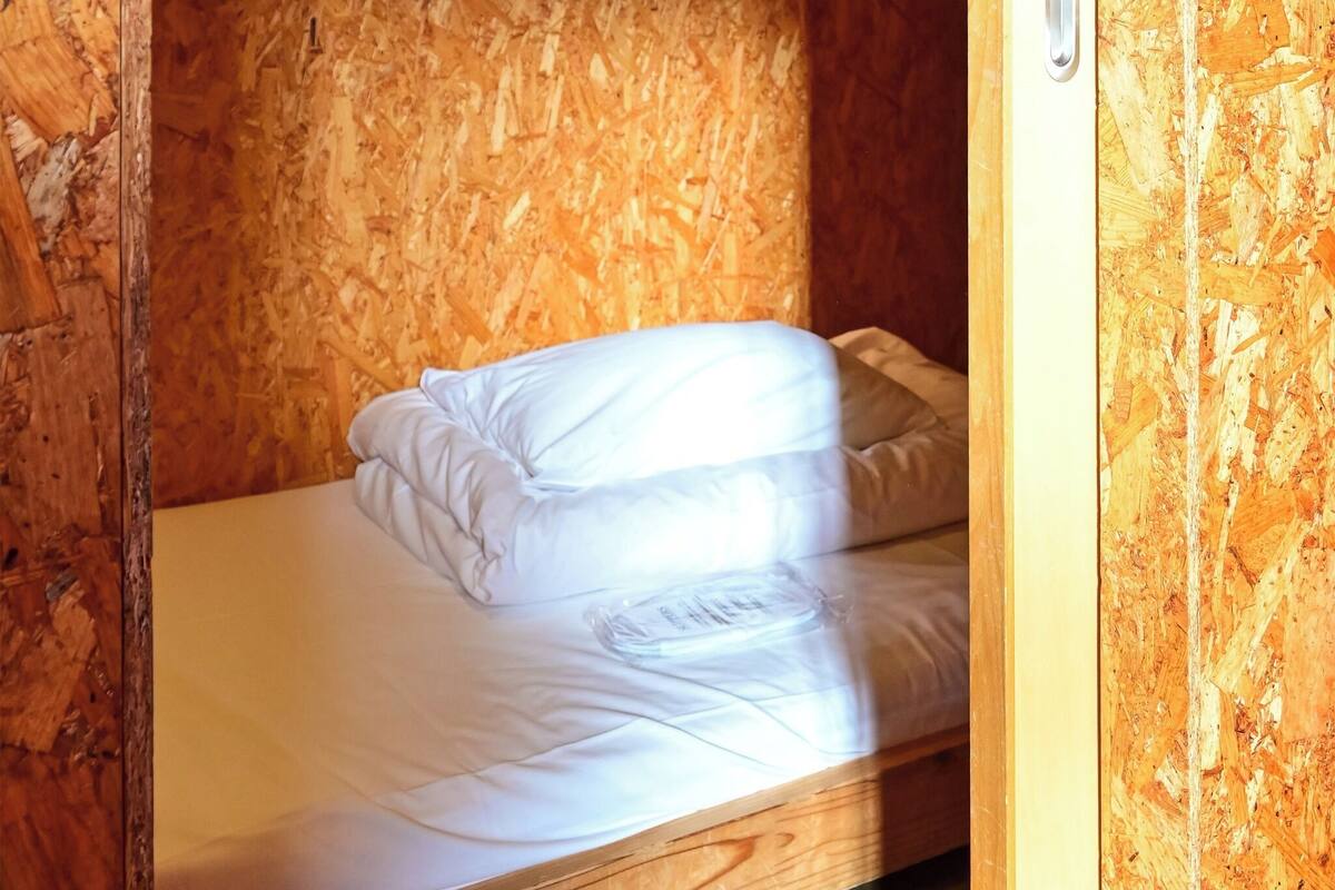 A single bed with white bedding in a room with wooden walls and a wooden floor.