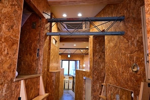 A narrow hallway with wooden walls and a mezzanine level with a metal beam structure. - Kawaramachi Dormitory - Hostel (Takamatsu)