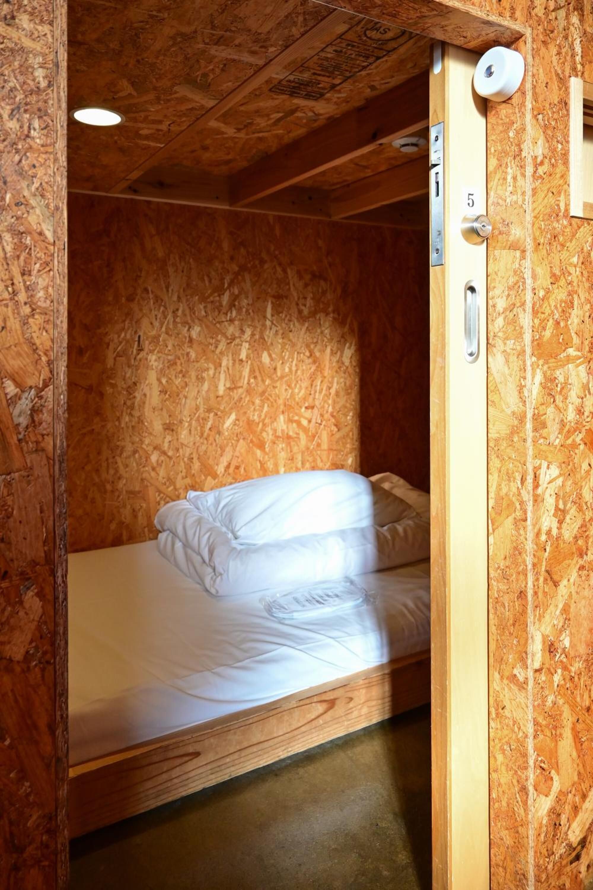 Habitación pequeña con cama individual, paredes de madera y puerta con placa de identificación.