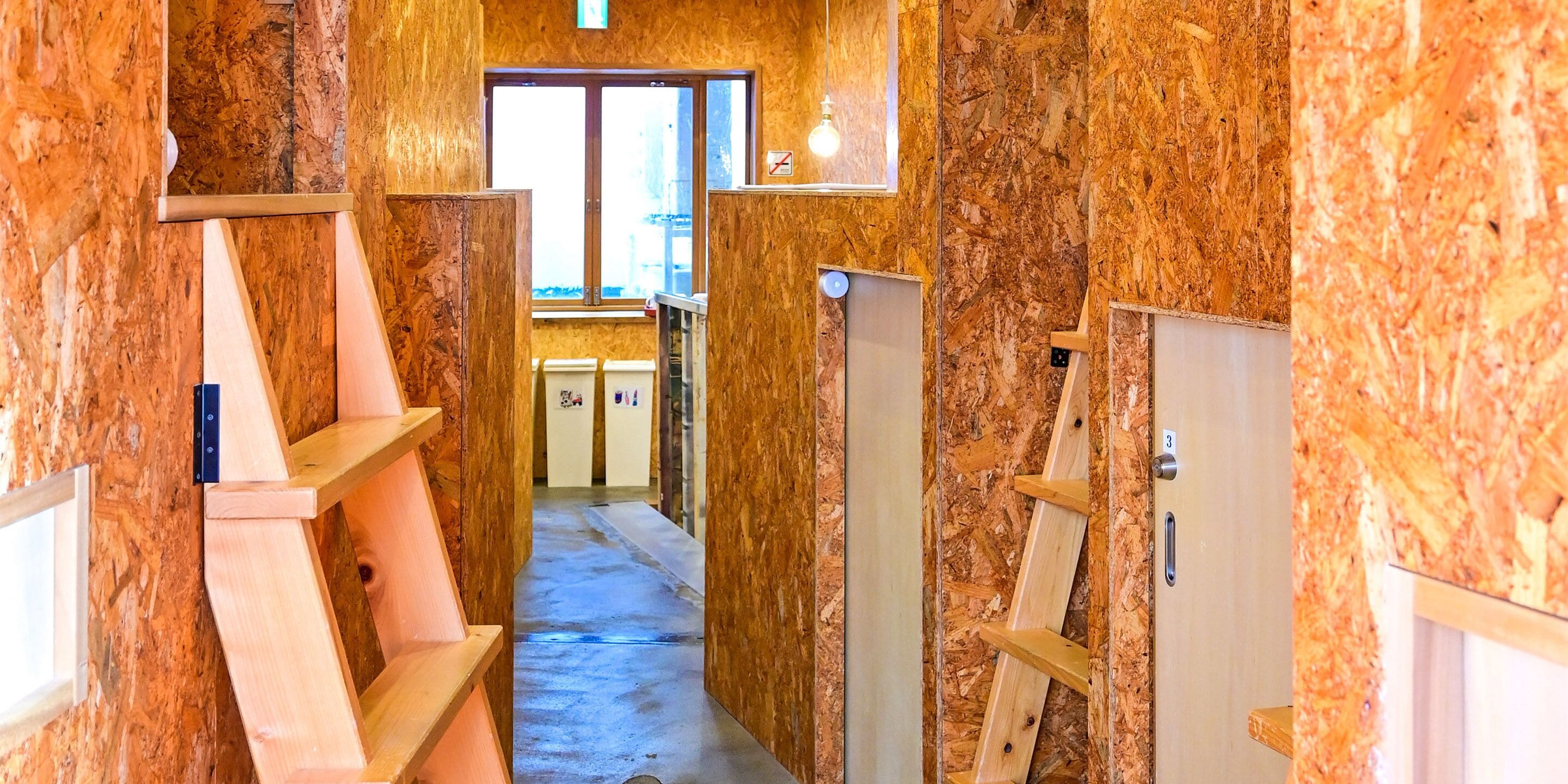 Un pasillo estrecho con paredes de madera y piso de concreto, que conduce a una zona de cocina con armarios y una ventana.