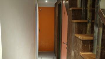 A narrow hallway with a wooden staircase on the right and an orange door at the end.