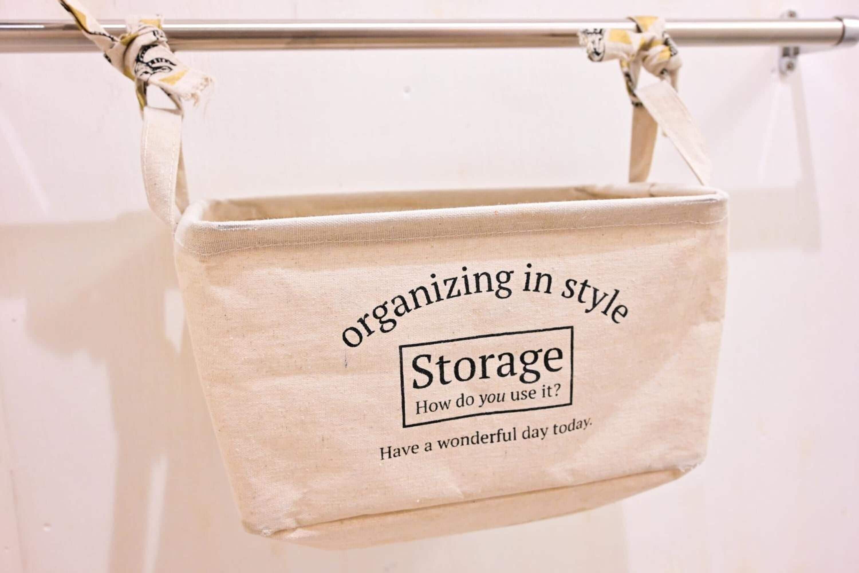 A beige canvas tote bag hanging on a metal rod, with text that reads "organizing in style Storage How do you use it? Have a wonderful day today."