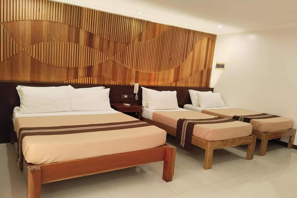 Habitación de hotel con tres camas, un cabecero de madera y una mesita de noche con lámpara.