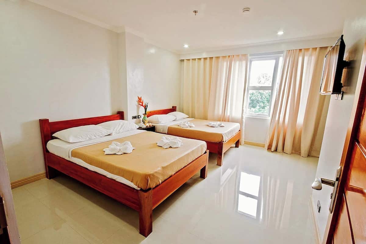 Habitación de hotel con dos camas de madera, sábanas blancas, una mesita con un florero y un ventanal con cortinas.
