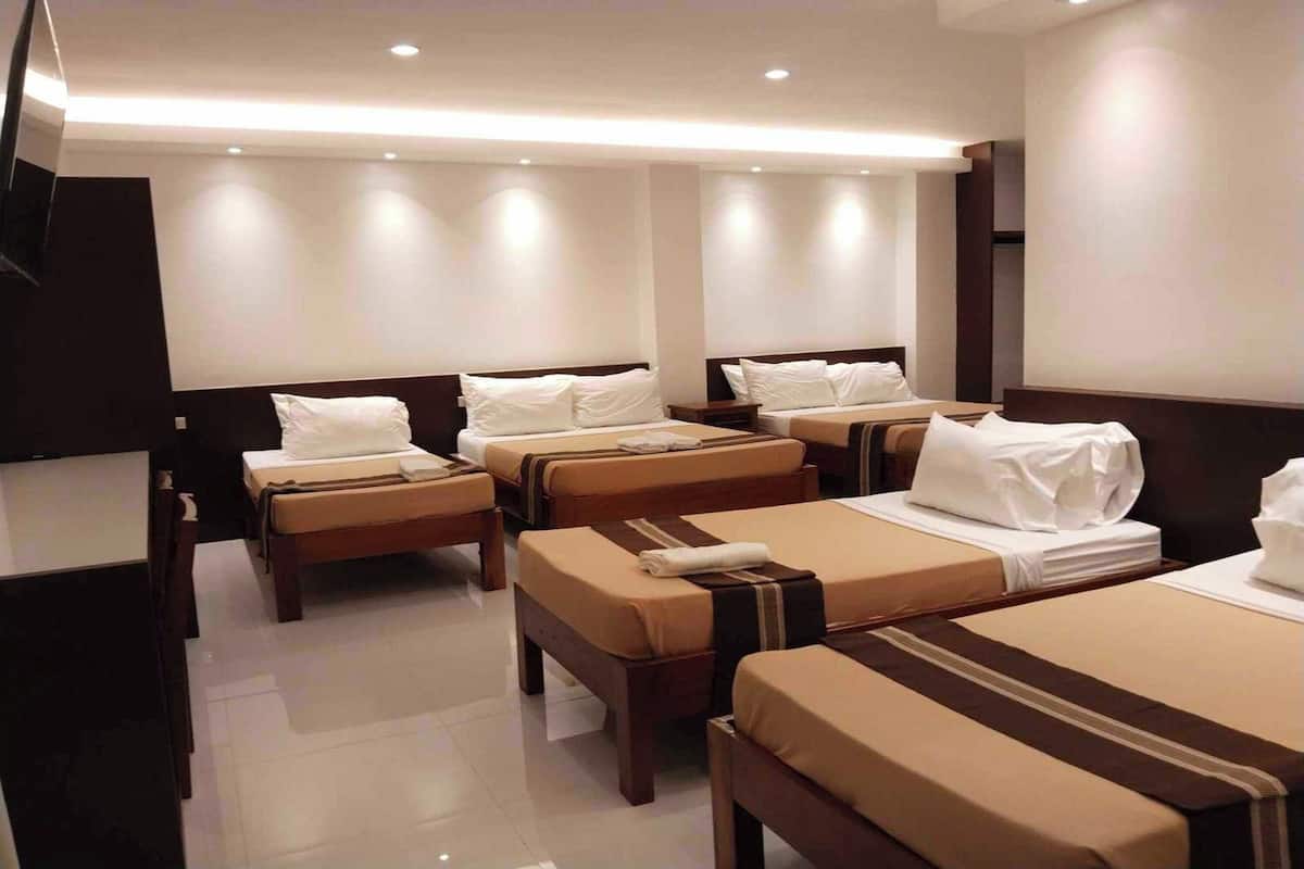 Habitación de hotel con cuatro camas individuales, un televisor de pantalla plana y un espejo grande.