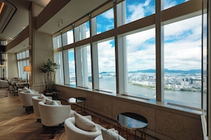 A modern hotel lobby with a long seating area, large windows, and a view of a cityscape. - Signiel Seoul (Seoul)