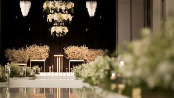 An indoor setting with a stage, floral arrangements, and chandeliers.