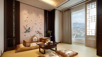 Una habitación con un ventanal grande que ofrece vistas a la ciudad, un conjunto de sofás de estilo tradicional, una mesa de centro de madera y una pared decorativa con motivos florales.