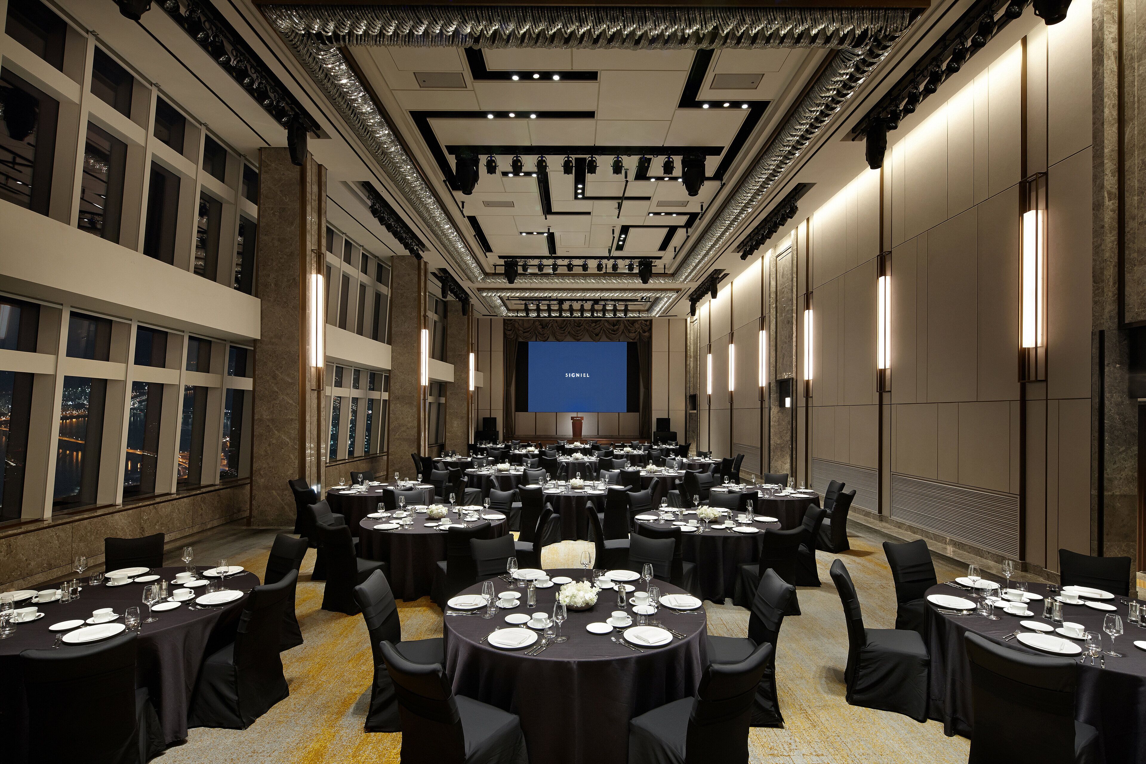 Un amplio salón de conferencias con varias mesas redondas dispuestas para comidas, equipado con sillas y vajilla.