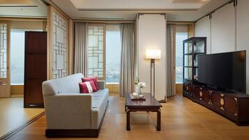 Una habitación de hotel moderna con sofá, una mesa de centro, televisión y vistas a la ciudad.