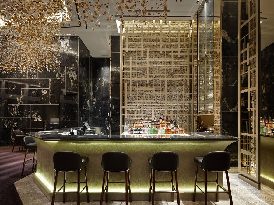 A bar area with a marble wall, a bar counter, and three black bar stools.