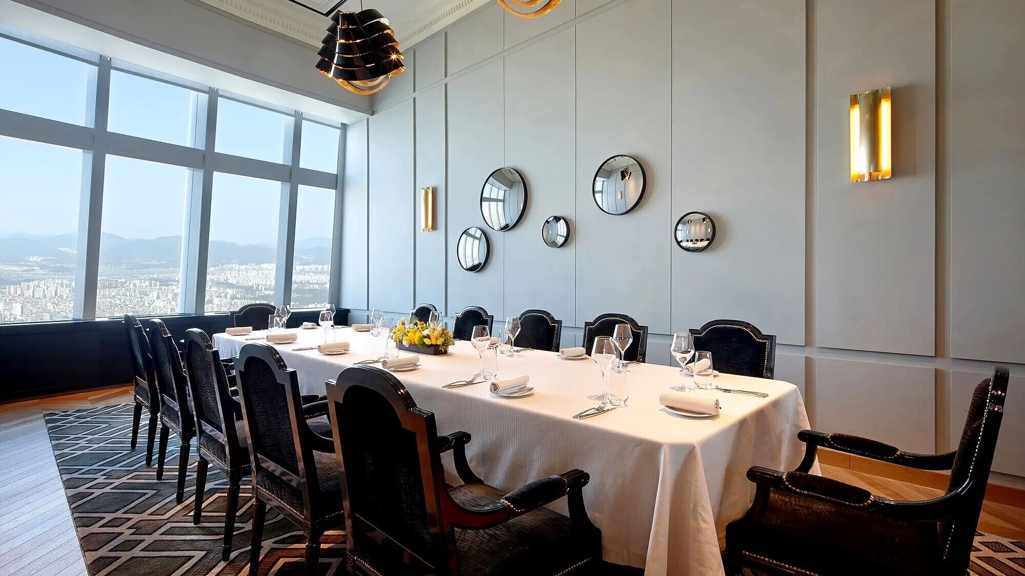 Comedor con mesa dispuesta para seis comensales, ventanas amplias y varios espejos en la pared.