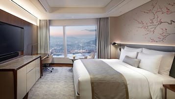 Una habitación de hotel moderna con una cama grande, un escritorio, una silla, un televisor y vistas a la ciudad a través de amplios ventanales.