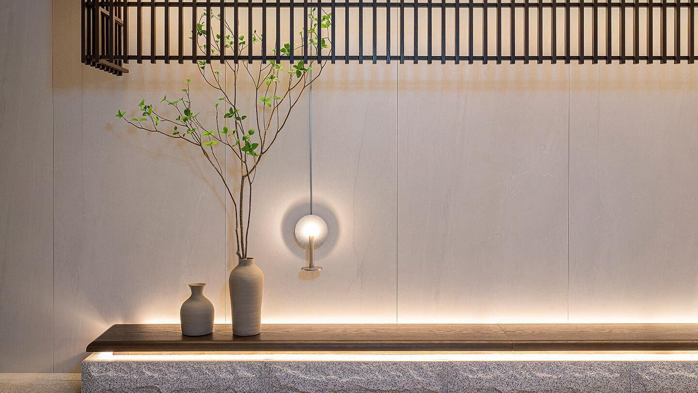 A minimalist interior with a wooden bench, two vases, and a wall-mounted light fixture.