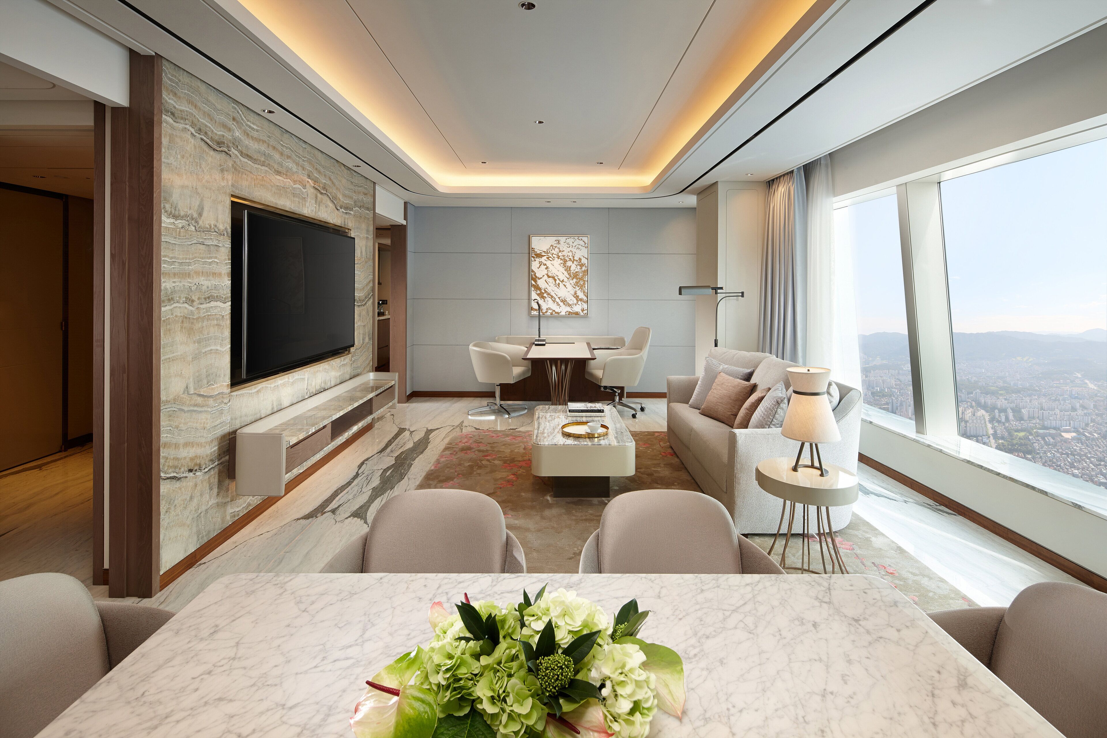 Una sala moderna con chimenea de mármol, televisor de pantalla plana, comedor con mesa de mármol y un ventanal con vistas a la ciudad.