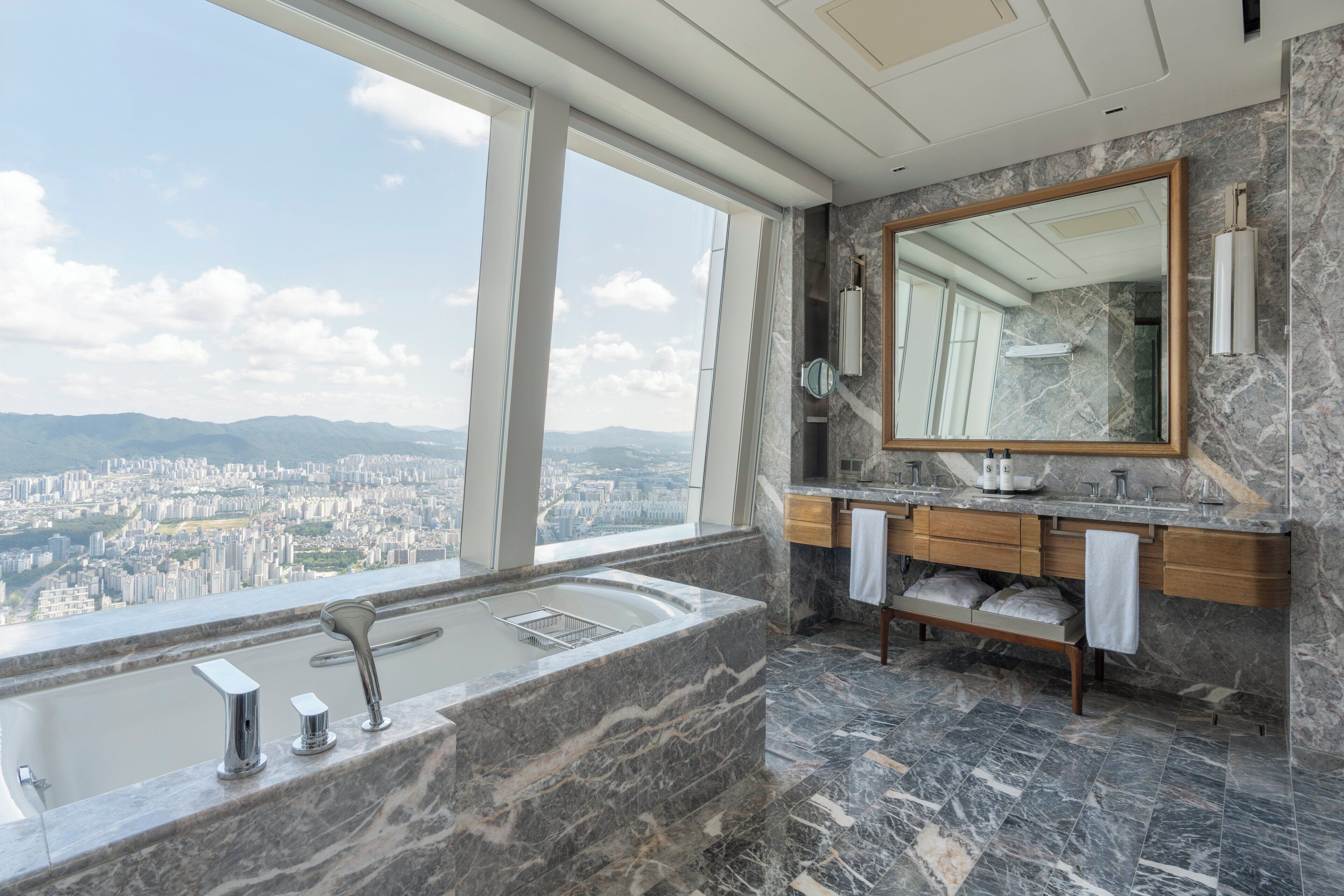 A modern bathroom with a large bathtub, a vanity with a mirror, and a view of a cityscape through large windows.