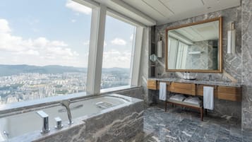 A modern bathroom with a large bathtub, a vanity with a mirror, and a view of a cityscape through large windows.