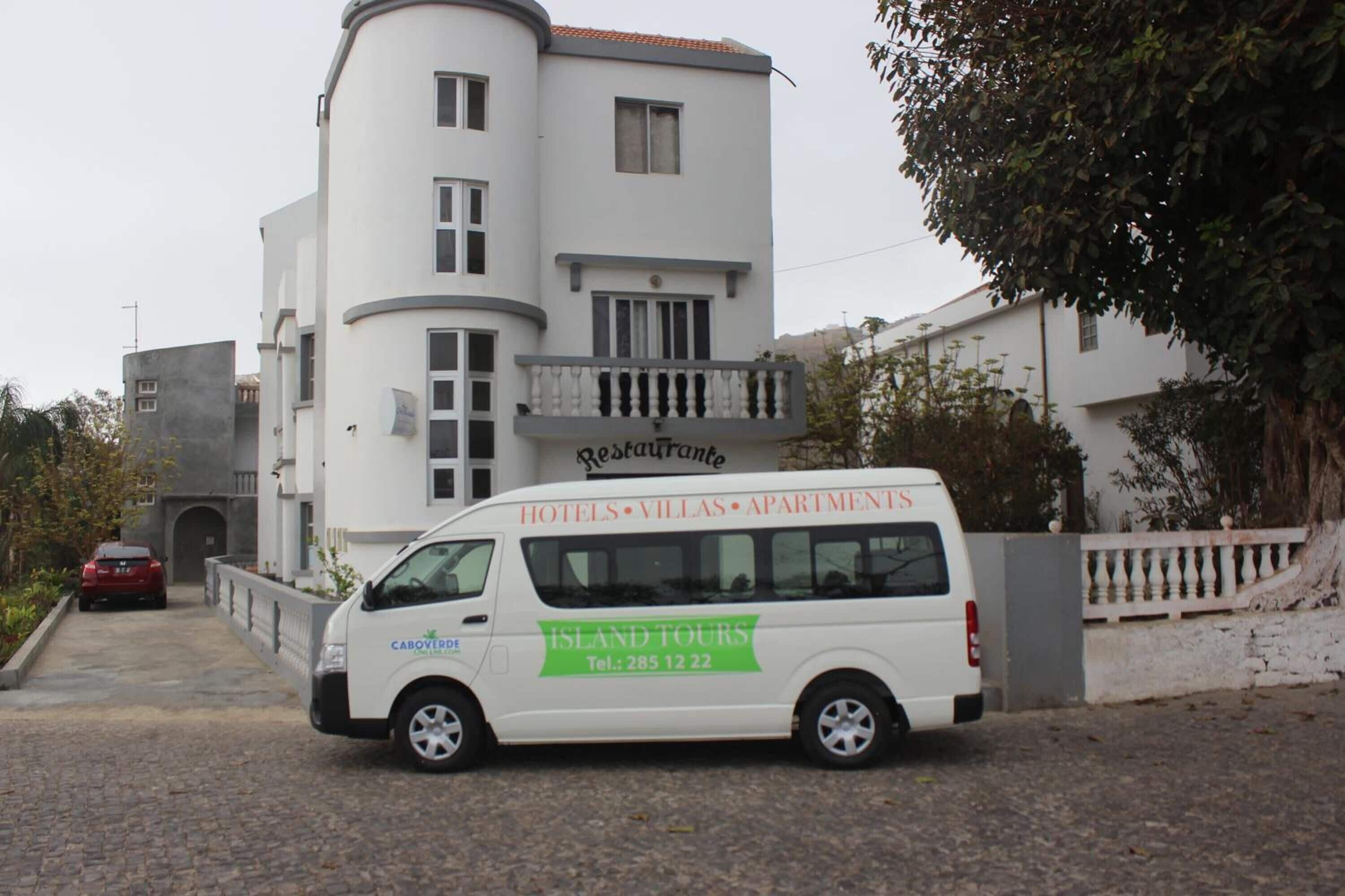 A white van parked in front of a building with a sign that reads "HOTELS, VILLAS, APARTMENTS."