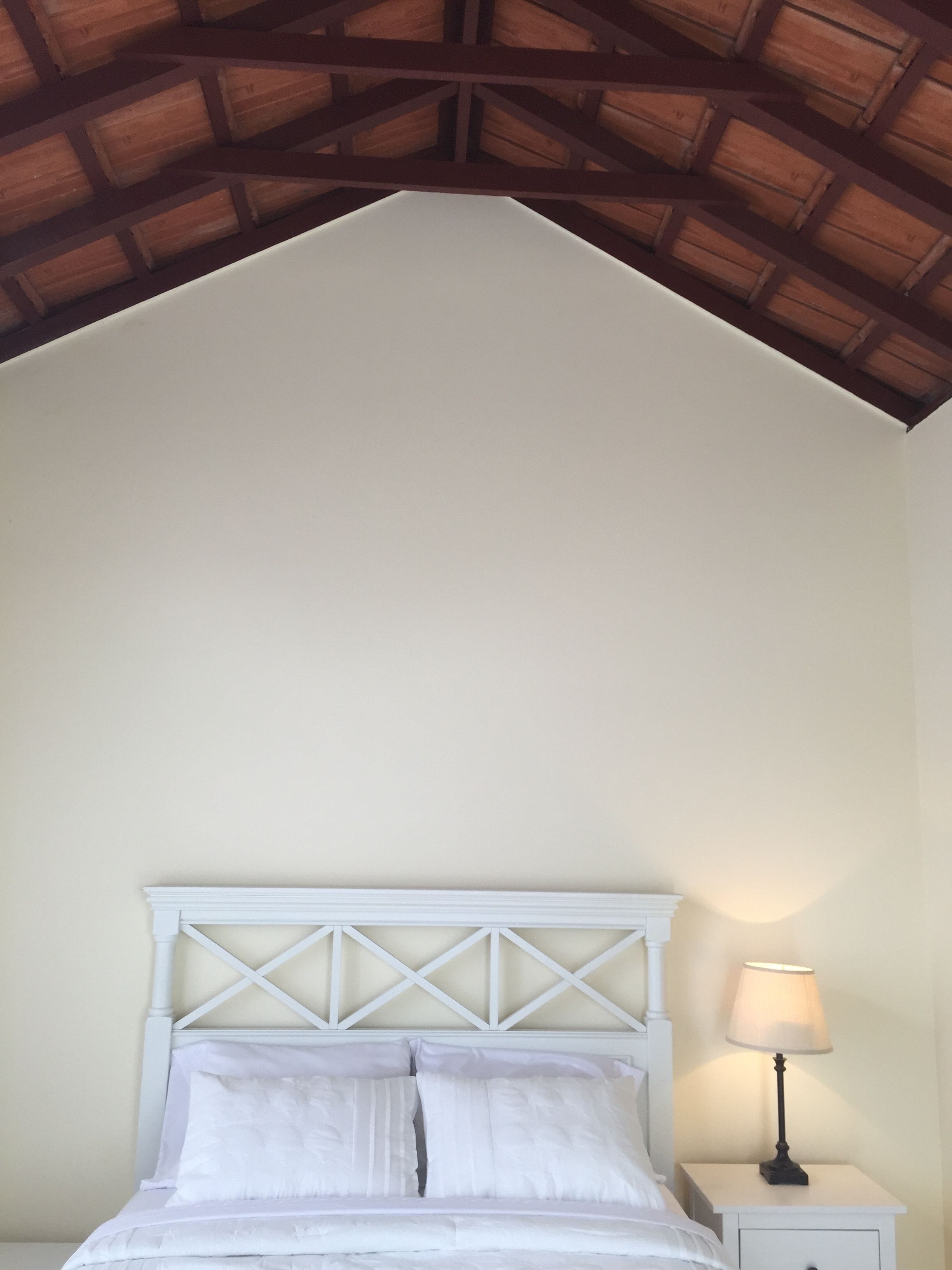 Un dormitorio con una cama blanca, una mesita de noche con lámpara y techo de madera.