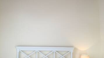 Un dormitorio con una cama blanca, una mesita de noche con lámpara y techo de madera.