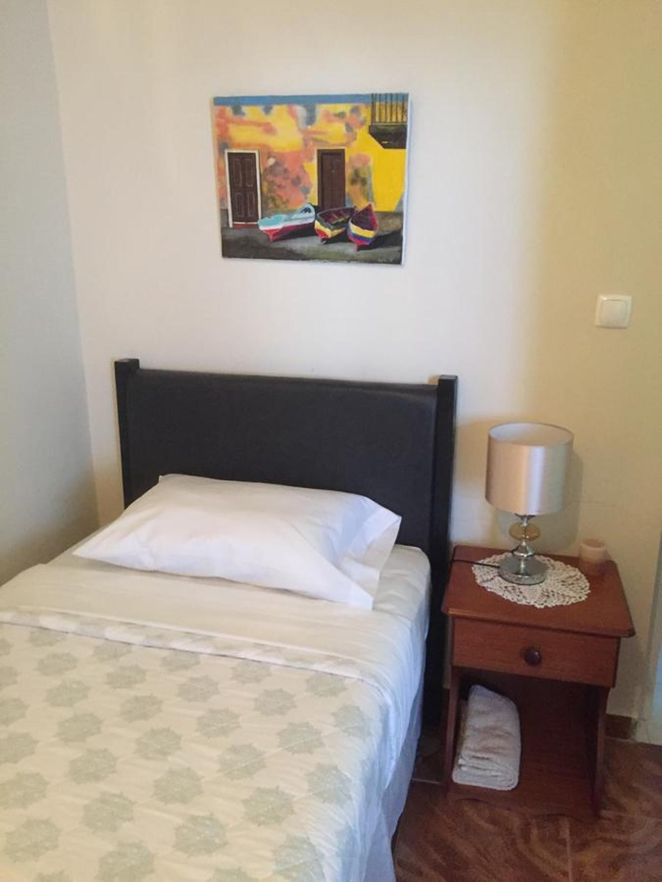Una cama bien hecha con una colcha estampada, un cabecero oscuro y un cuadro colgado en la pared.