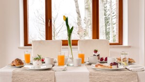 Une table mise pour le petit-déjeuner, avec deux chaises, une table garnie d’assiettes de nourriture, des verres de jus d’orange et un vase contenant une seule fleur.