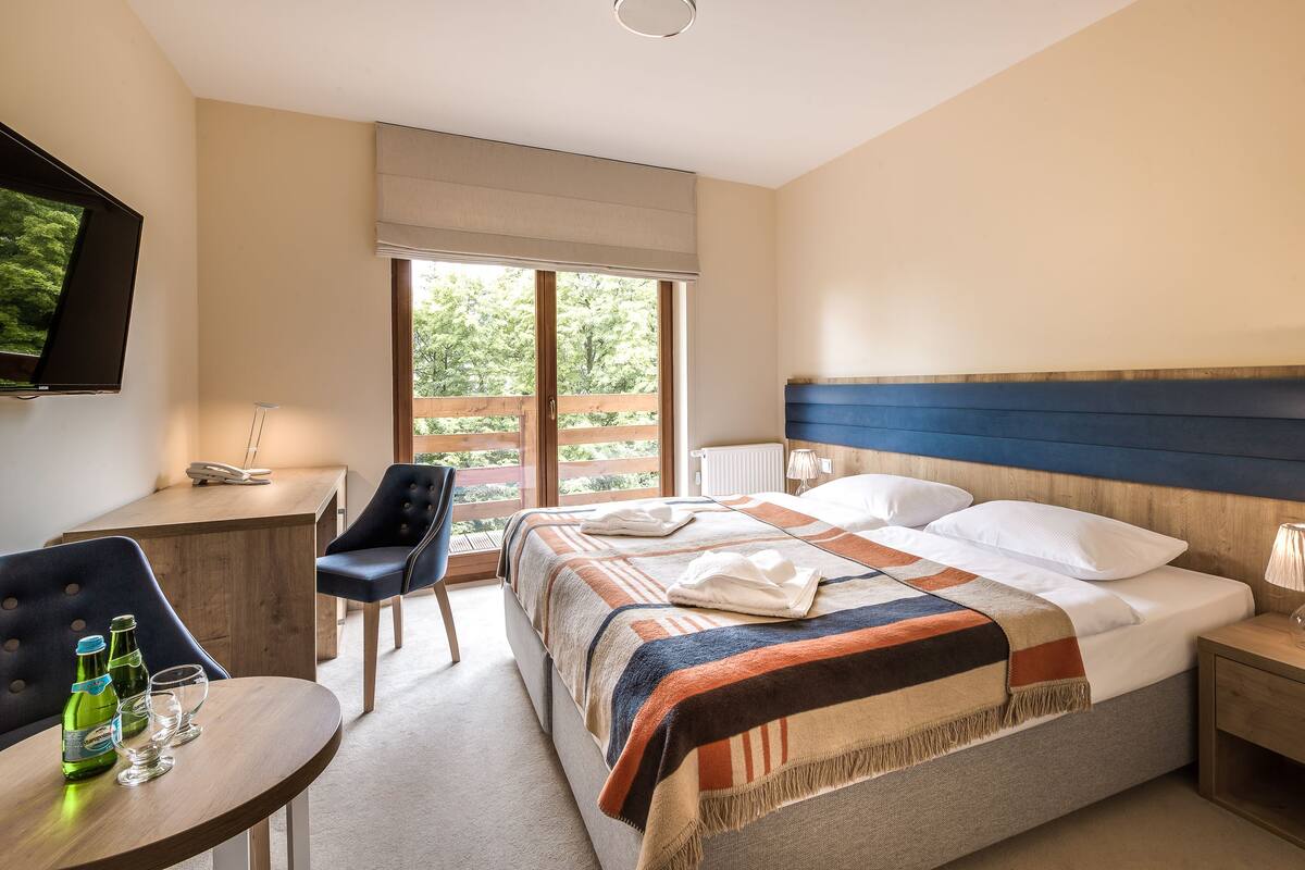 A hotel room with a bed, bedside table, chair, and a desk with a chair.
