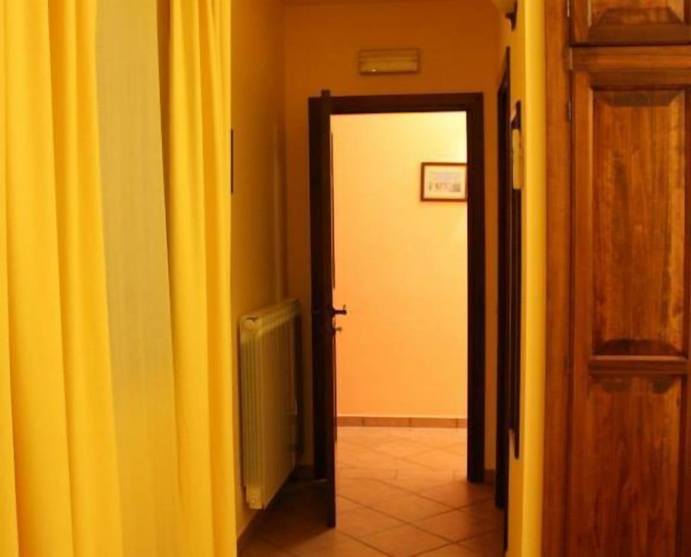 Un couloir étroit avec des rideaux jaunes, un radiateur et une porte en bois donnant sur une pièce.