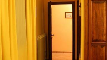 A narrow hallway with yellow curtains, a radiator, and a wooden door leading to a room.