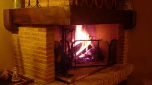 Una chimenea de ladrillo con fuego ardiendo en su interior, una rejilla de metal sobre el fuego y un repisa de madera.