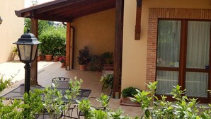 Un patio techado con mesa y sillas, plantas en macetas y un farol.