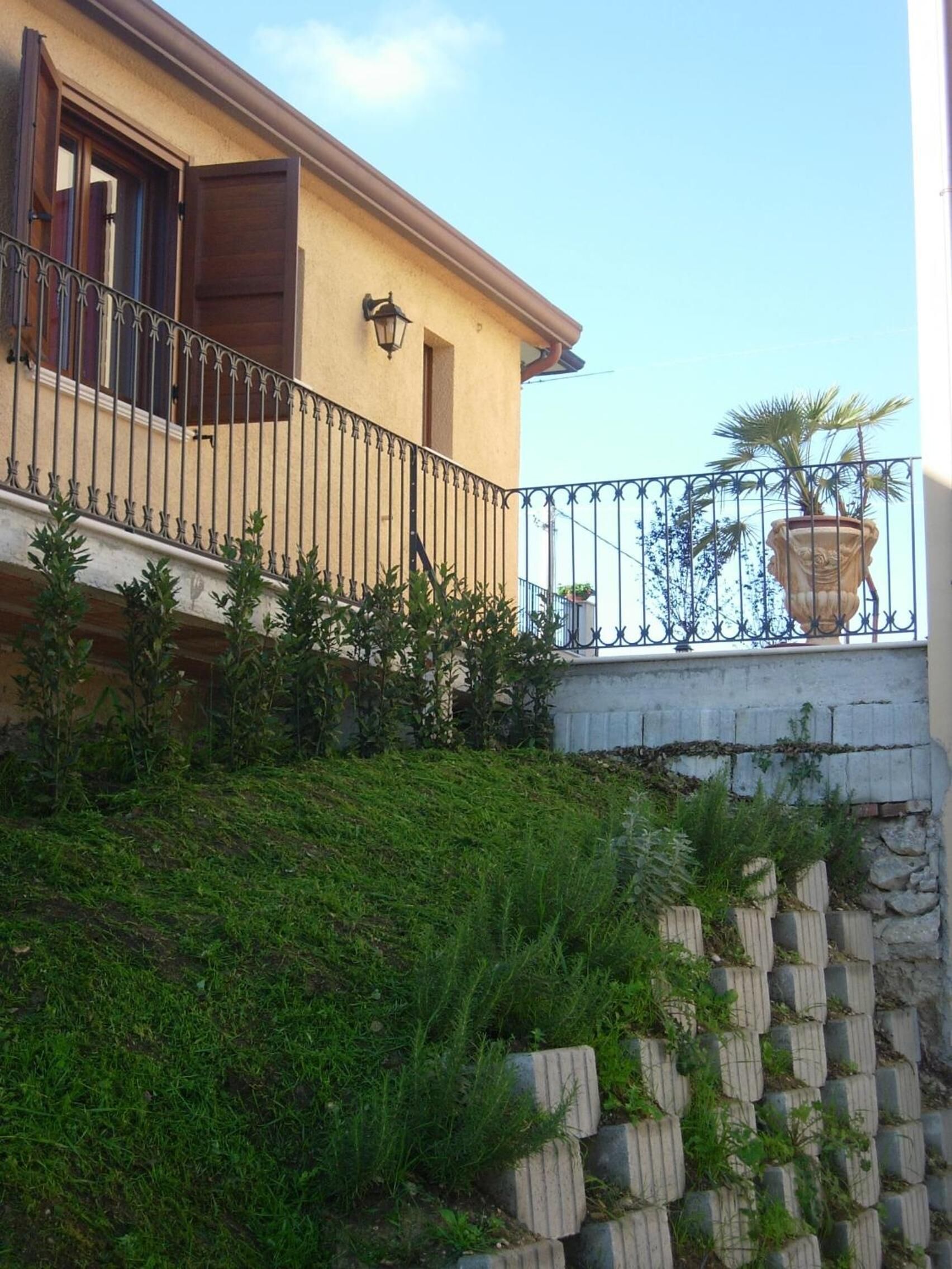 Un edificio a due piani con un balcone, un muro di sostegno in pietra e una pianta in vaso.