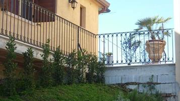 Un edificio a due piani con un balcone, un muro di sostegno in pietra e una pianta in vaso.