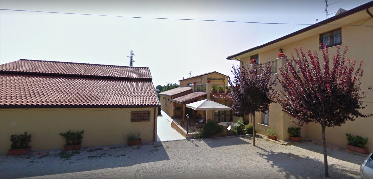 Ein Gebäude mit einem Ziegeldach, einem Schild mit der Aufschrift 'Angelo' und einem Baum mit roten Blüten.