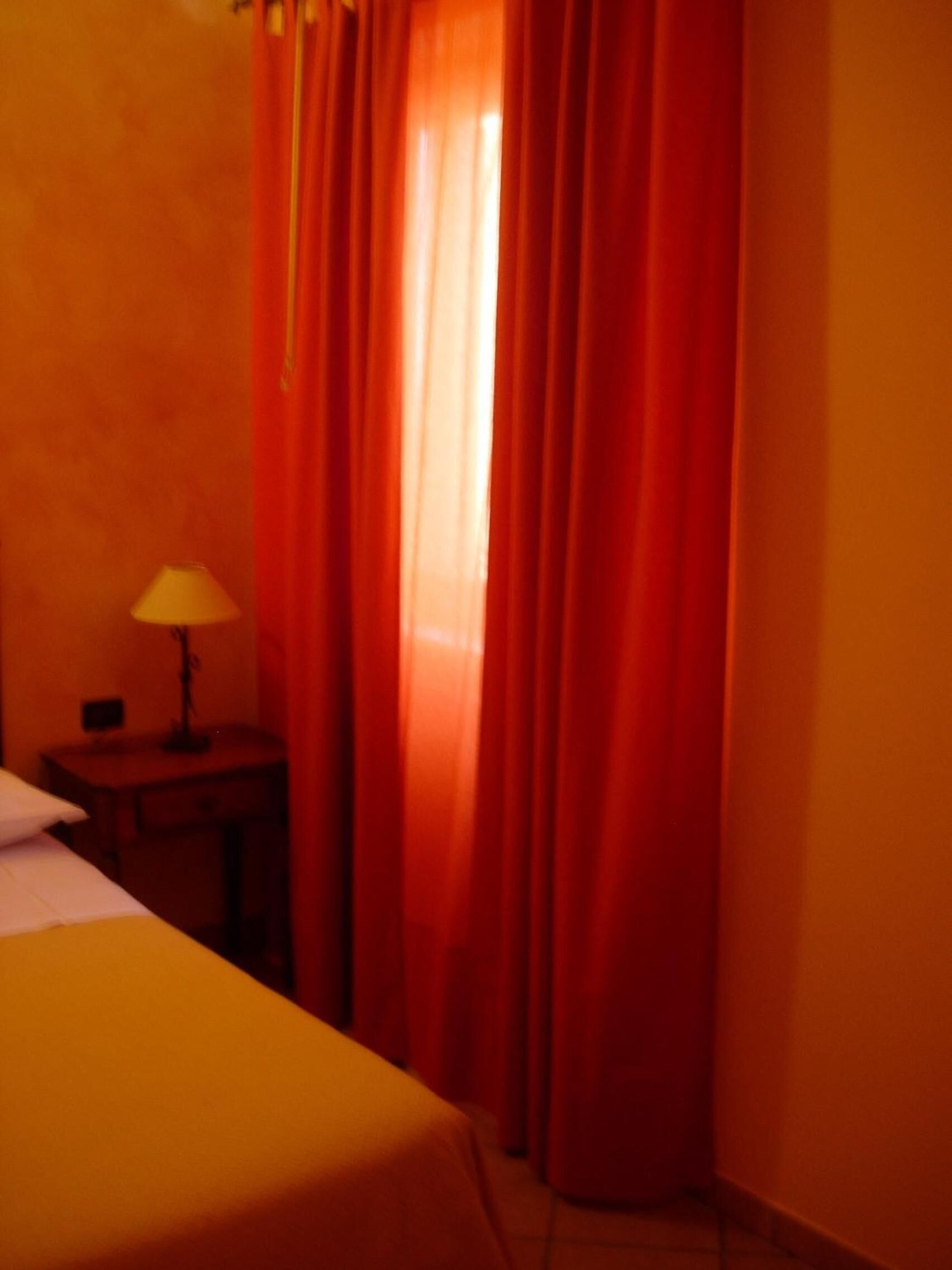 Una habitación de hotel con cama, mesita de noche, lámpara y cortinas rojas.