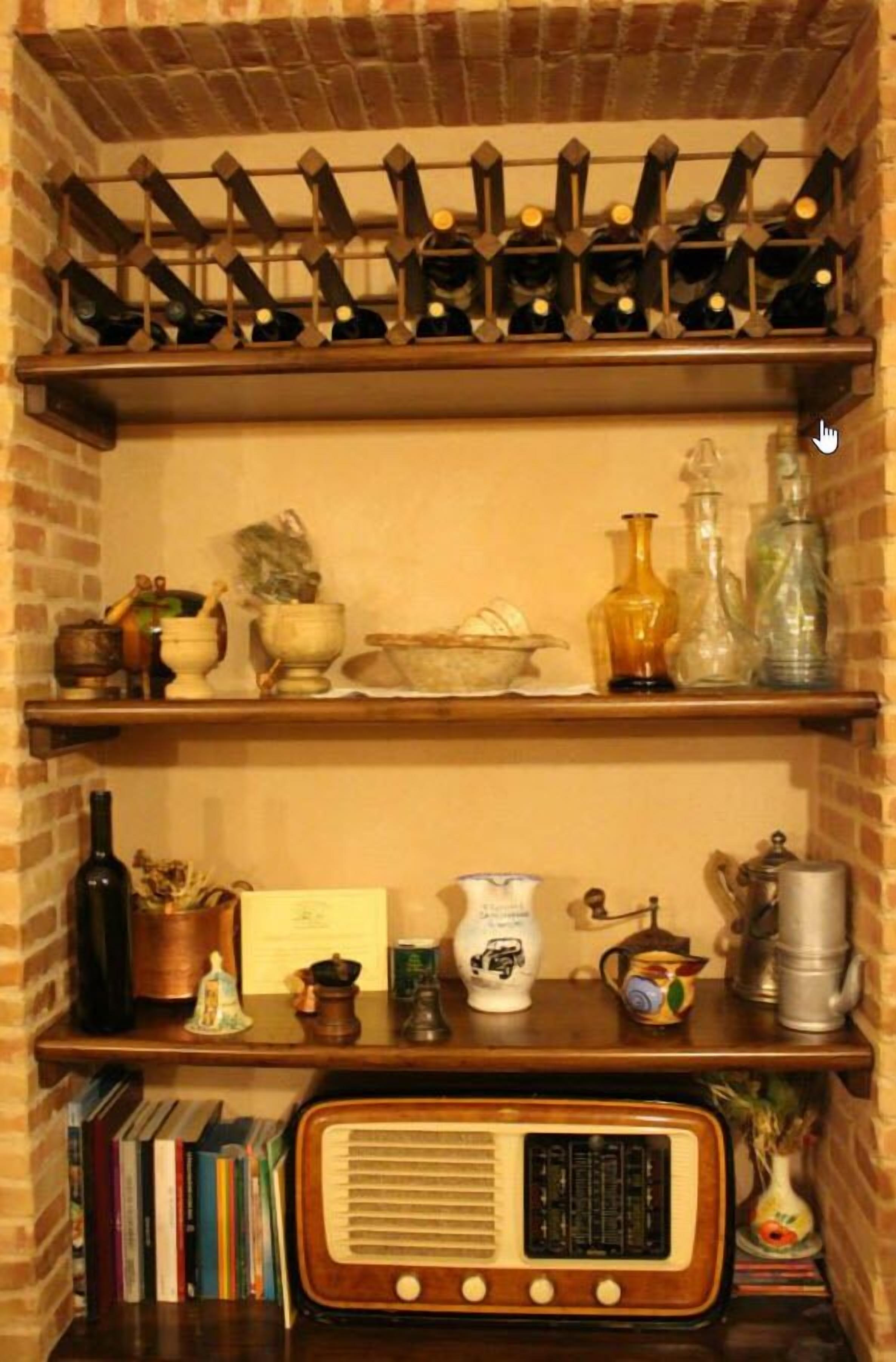 Un mur en briques avec des étagères où sont rangées des bouteilles de vin, des ustensiles de cuisine et une radio ancienne.