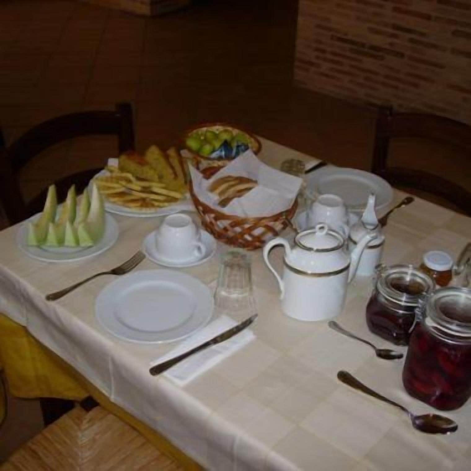 A breakfast table set with plates, cutlery, a teapot, a fruit bowl, and condiments.