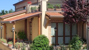 Una casa de dos pisos con balcón, plantas en macetas y un jardín bien cuidado.