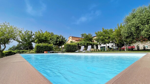 Una piscina con cubierta de madera, rodeada de vegetación y edificios.