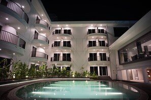 A modern hotel with multiple balconies, a central swimming pool, and indoor plants.