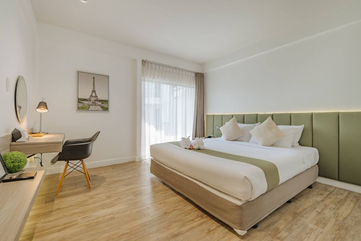 A hotel room with a large bed, a desk with a chair, a lamp, and a picture of the Eiffel Tower on the wall.
