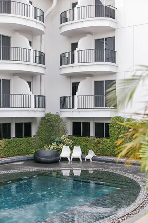 A modern building with multiple balconies, a swimming pool, and outdoor seating.