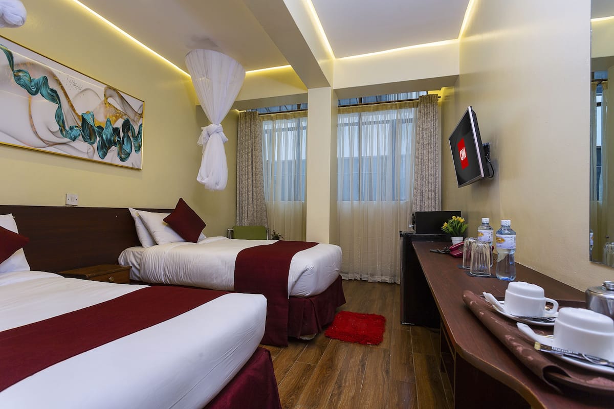 Habitación de hotel con dos camas, un escritorio con computadora, un televisor y un cuadro abstracto grande en la pared.