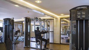 A gym with various exercise machines, a mirrored wall, and a ceiling with recessed lighting.