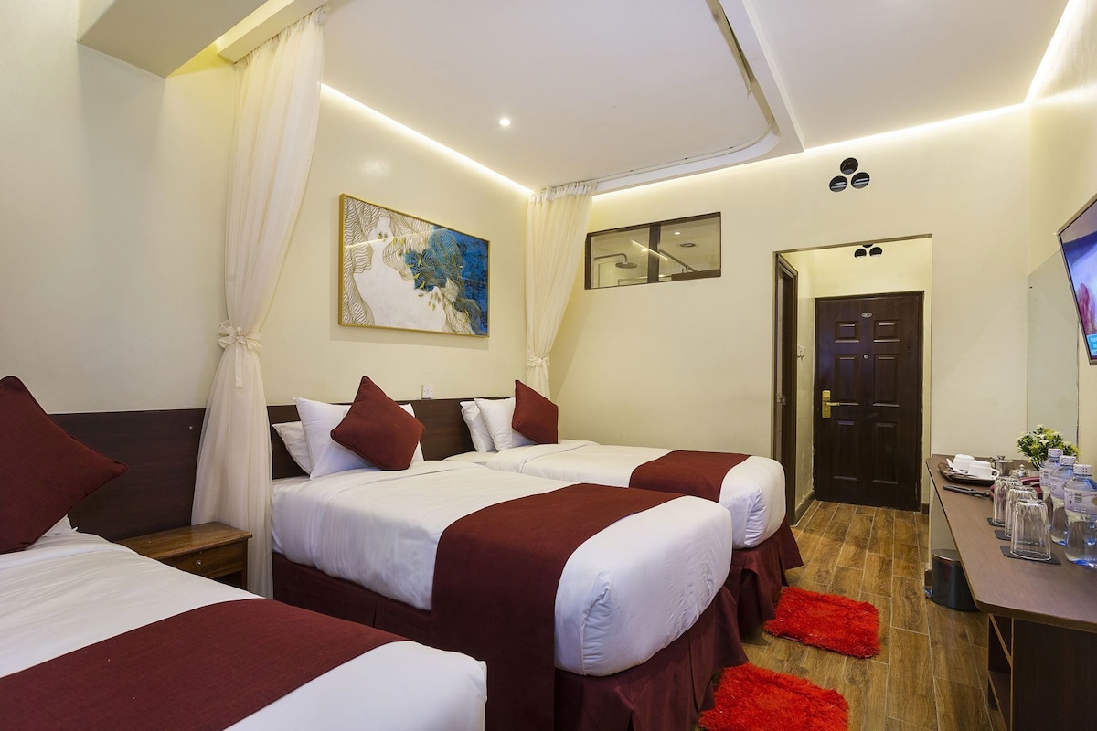 A hotel room with two beds, a desk, a TV, and a door.