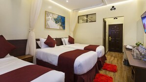 A hotel room with two beds, a desk with amenities, a painting, and a door.