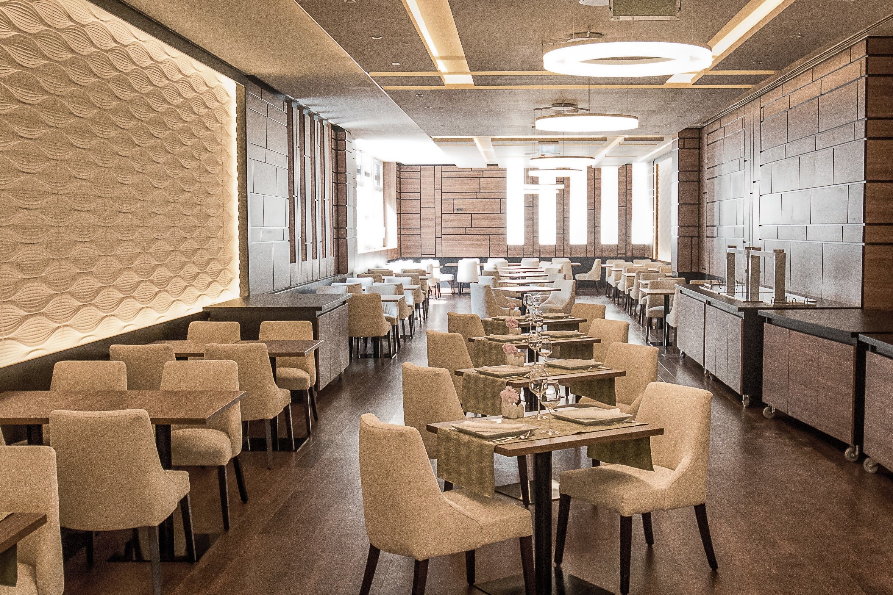 A modern restaurant with a long counter, multiple tables, and chairs.